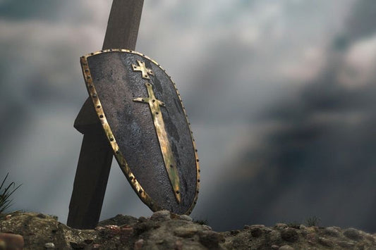 A shield and sword resting on a rocky ground with a cloudy backdrop, representing strength and faith. Be Still and know that He is God.